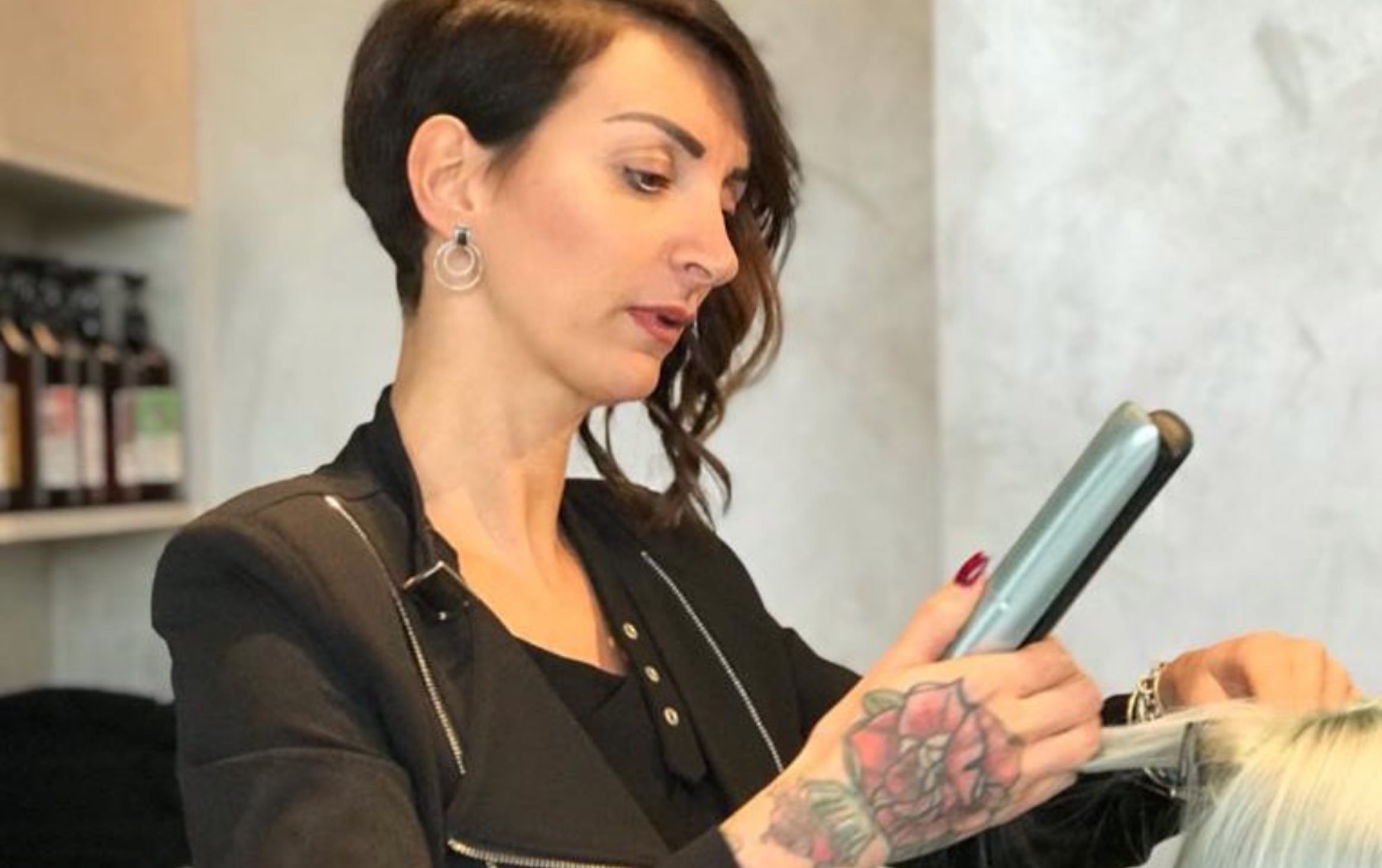 Parrucchiera con tatuaggio lavora a una acconciatura